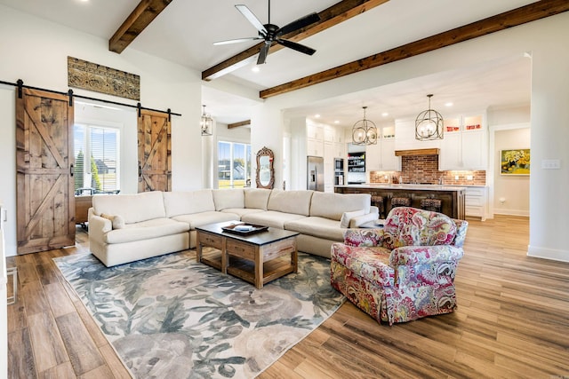 living room with beam ceiling, a barn door, ceiling fan, and light hardwood / wood-style floors