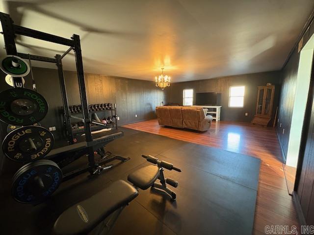 exercise room featuring hardwood / wood-style flooring, wood walls, and an inviting chandelier