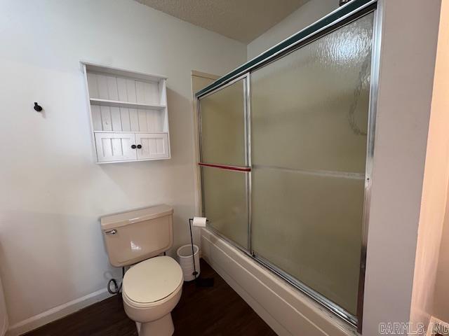 bathroom featuring hardwood / wood-style flooring, enclosed tub / shower combo, and toilet