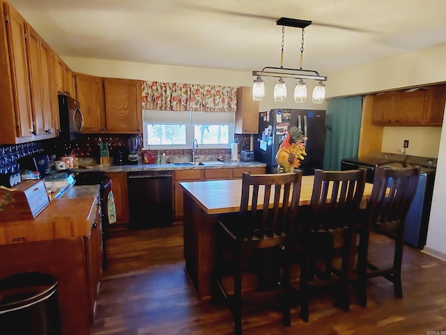 kitchen featuring pendant lighting, black appliances, sink, a kitchen island, and dark hardwood / wood-style flooring