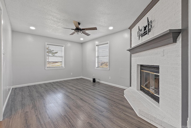 unfurnished living room with a wealth of natural light, a textured ceiling, ceiling fan, dark wood-type flooring, and a fireplace