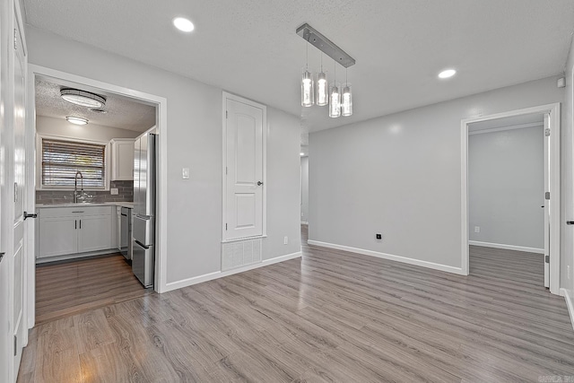 interior space featuring sink, hanging light fixtures, stainless steel appliances, light hardwood / wood-style floors, and white cabinets