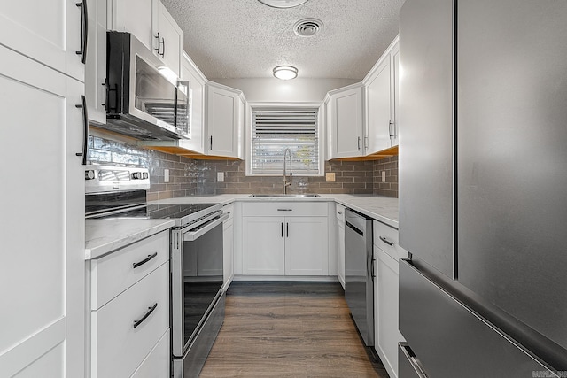 kitchen featuring appliances with stainless steel finishes, backsplash, dark wood-type flooring, sink, and white cabinetry