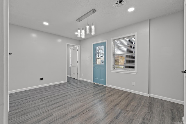 empty room with a notable chandelier, dark hardwood / wood-style flooring, and a textured ceiling