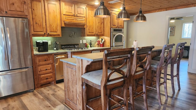 kitchen with wooden ceiling, decorative backsplash, an island with sink, appliances with stainless steel finishes, and decorative light fixtures