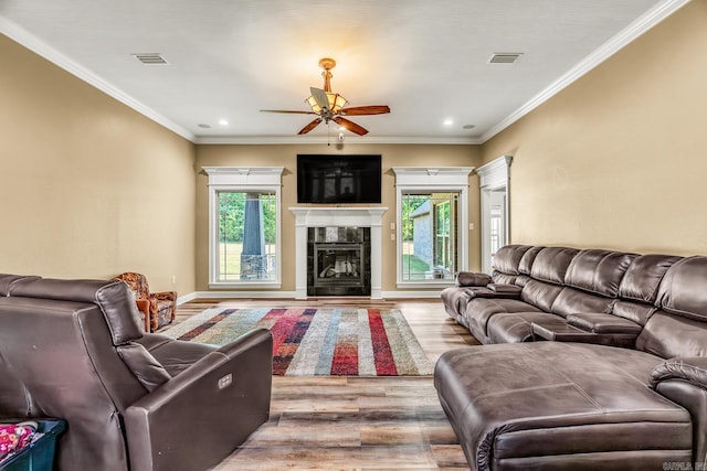 living room featuring ceiling fan, light hardwood / wood-style floors, ornamental molding, and a tiled fireplace