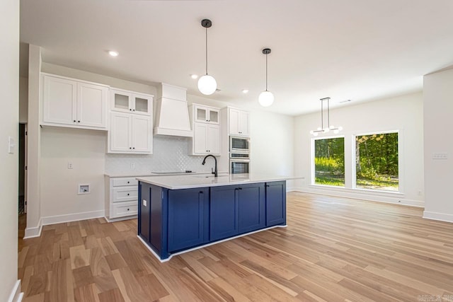 kitchen with white cabinets, custom exhaust hood, hanging light fixtures, and appliances with stainless steel finishes