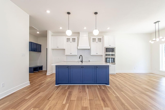 kitchen featuring custom exhaust hood, oven, blue cabinetry, built in microwave, and white cabinetry