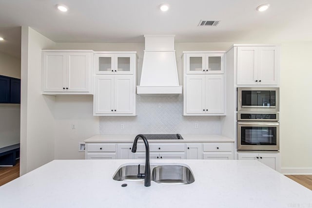 kitchen featuring custom range hood, stainless steel appliances, white cabinetry, and sink