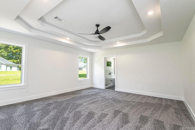 empty room featuring carpet flooring, ceiling fan, a raised ceiling, and a wealth of natural light