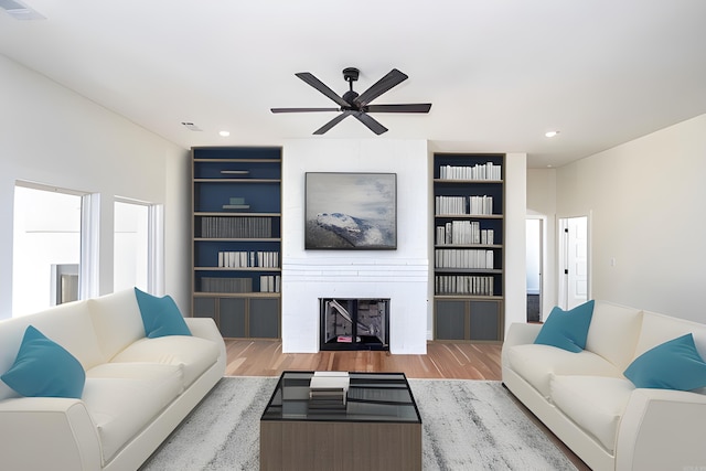 living room featuring built in shelves, ceiling fan, a large fireplace, and wood-type flooring