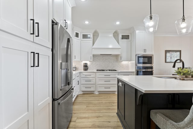 kitchen with stainless steel appliances, light countertops, custom range hood, glass insert cabinets, and white cabinets