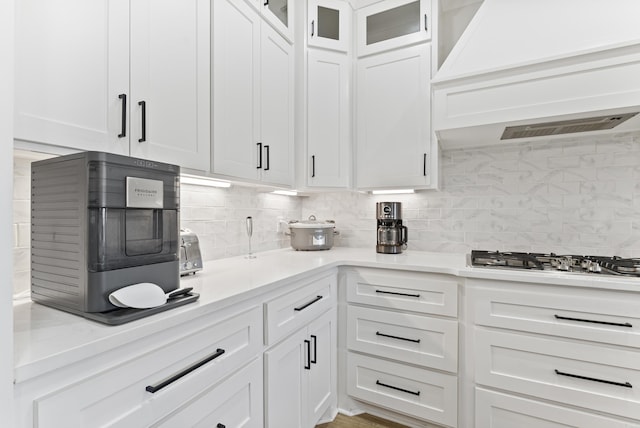 kitchen featuring light countertops, custom range hood, backsplash, glass insert cabinets, and white cabinets