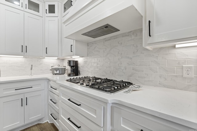 kitchen with stainless steel gas cooktop, white cabinets, light countertops, custom exhaust hood, and glass insert cabinets