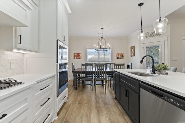 kitchen with a sink, white cabinetry, light countertops, appliances with stainless steel finishes, and hanging light fixtures