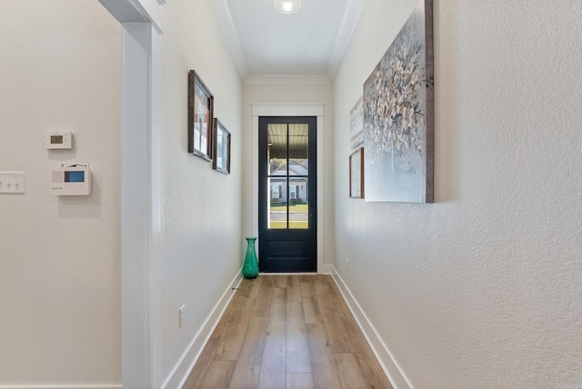 entryway featuring ornamental molding, a textured wall, light wood-style flooring, and baseboards