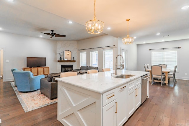 kitchen with a kitchen island with sink, white cabinets, sink, hanging light fixtures, and a fireplace