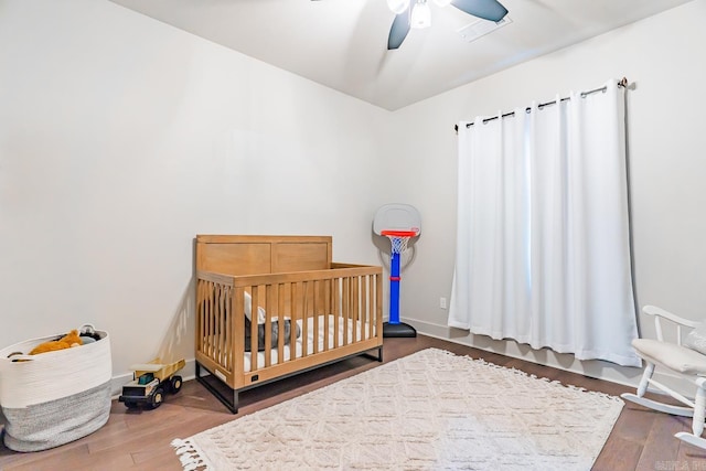 bedroom with a crib, hardwood / wood-style flooring, and ceiling fan