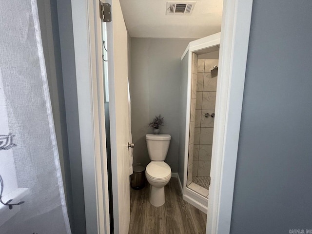 bathroom with tiled shower, wood-type flooring, and toilet