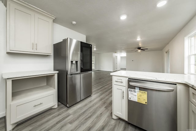 kitchen with light stone countertops, appliances with stainless steel finishes, light wood-type flooring, and ceiling fan