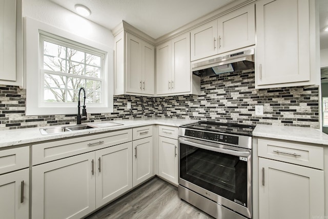 kitchen featuring sink, stainless steel stove, decorative backsplash, light wood-type flooring, and light stone countertops