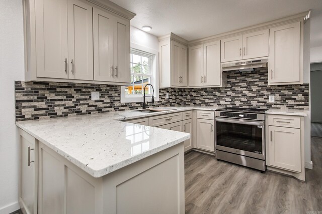 kitchen featuring light stone countertops, backsplash, sink, stainless steel range oven, and light hardwood / wood-style floors