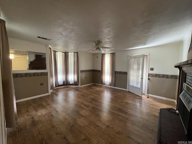 unfurnished living room with a textured ceiling, ceiling fan, hardwood / wood-style flooring, a fireplace, and plenty of natural light