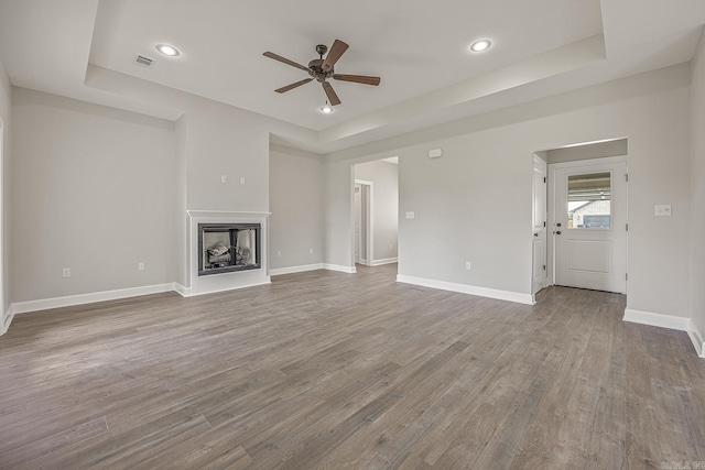 unfurnished living room with a tray ceiling, ceiling fan, and hardwood / wood-style flooring