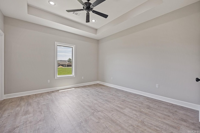 spare room with a raised ceiling, ceiling fan, and light wood-type flooring