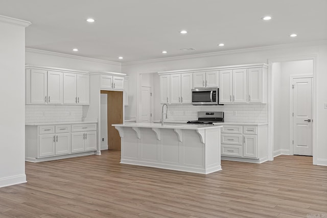 kitchen with white cabinetry, a kitchen island with sink, light wood-type flooring, and appliances with stainless steel finishes