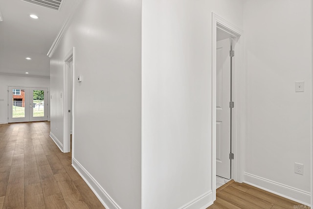 corridor with french doors, ornamental molding, and light wood-type flooring