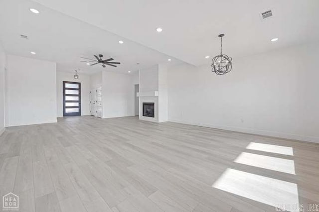 unfurnished living room with ceiling fan with notable chandelier, light hardwood / wood-style floors, and a fireplace