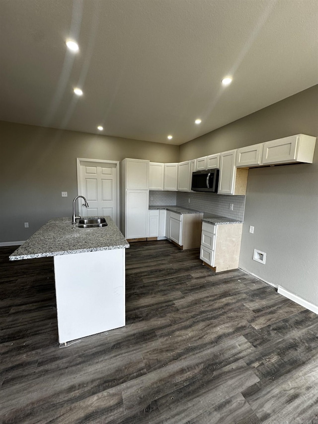 kitchen with dark wood-type flooring, sink, light stone counters, a center island with sink, and white cabinets