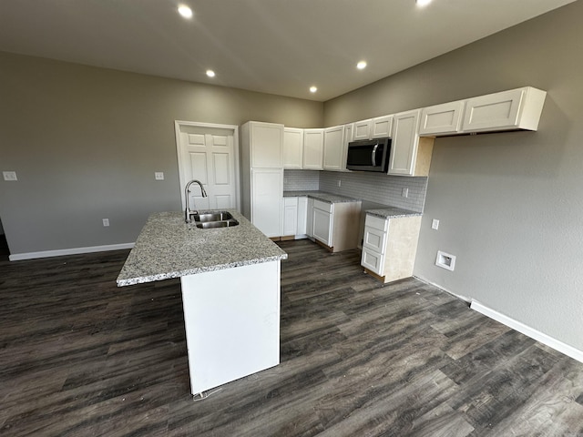 kitchen featuring white cabinetry, a kitchen island with sink, sink, and light stone counters