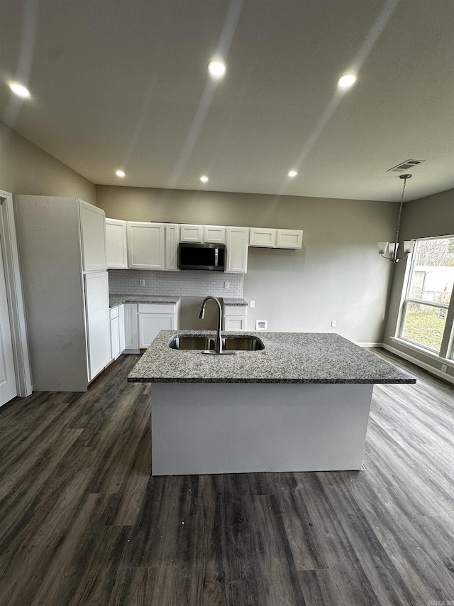 kitchen with sink, white cabinetry, backsplash, dark stone countertops, and an island with sink