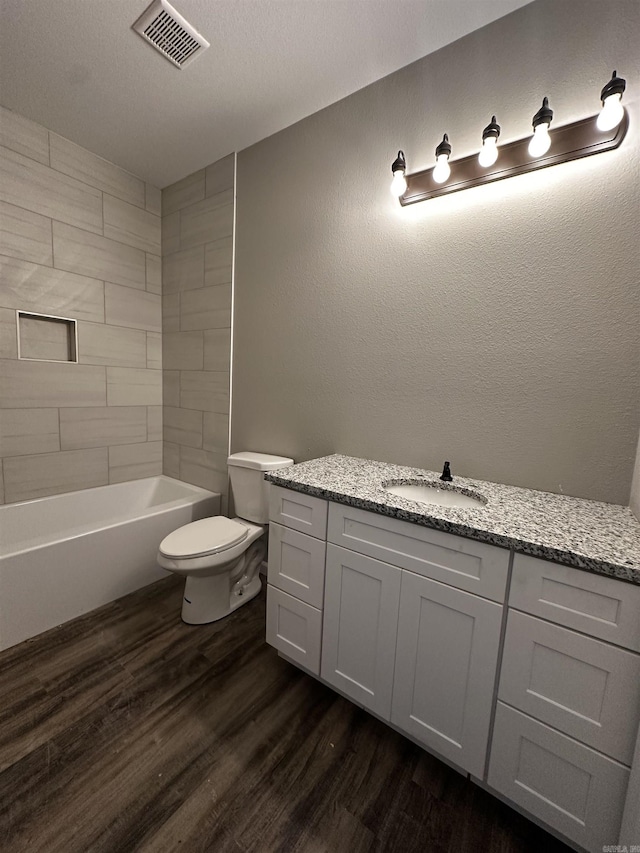 full bathroom with toilet, tiled shower / bath, wood-type flooring, a textured ceiling, and vanity