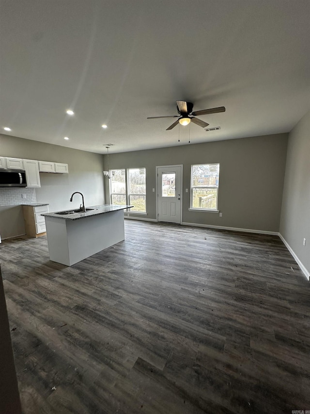 kitchen featuring open floor plan, stainless steel microwave, white cabinetry, and an island with sink