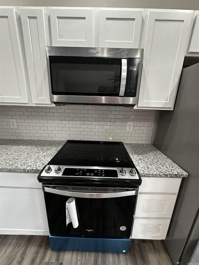 kitchen with dark hardwood / wood-style floors, backsplash, white cabinets, light stone counters, and stainless steel appliances