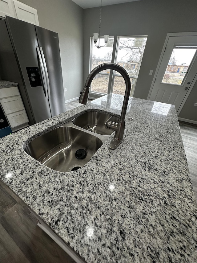 details with pendant lighting, light stone countertops, sink, and stainless steel fridge with ice dispenser