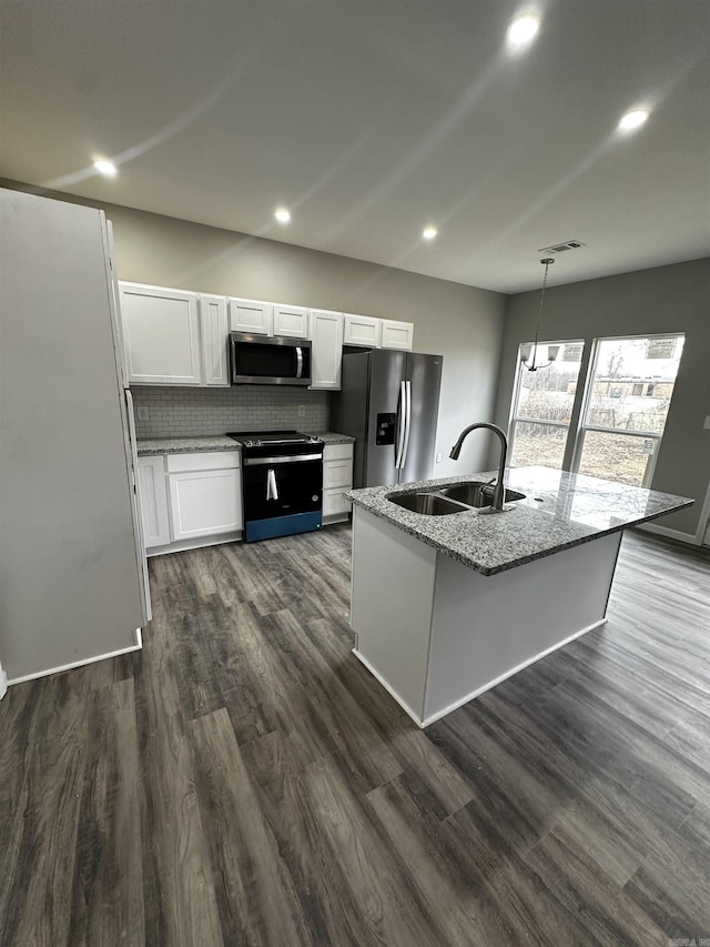 kitchen featuring appliances with stainless steel finishes, white cabinetry, sink, light stone countertops, and a center island with sink