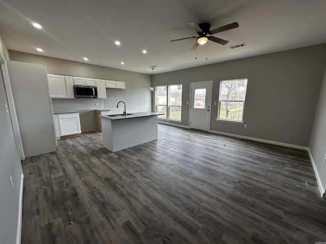 kitchen with ceiling fan, white cabinetry, hanging light fixtures, backsplash, and an island with sink