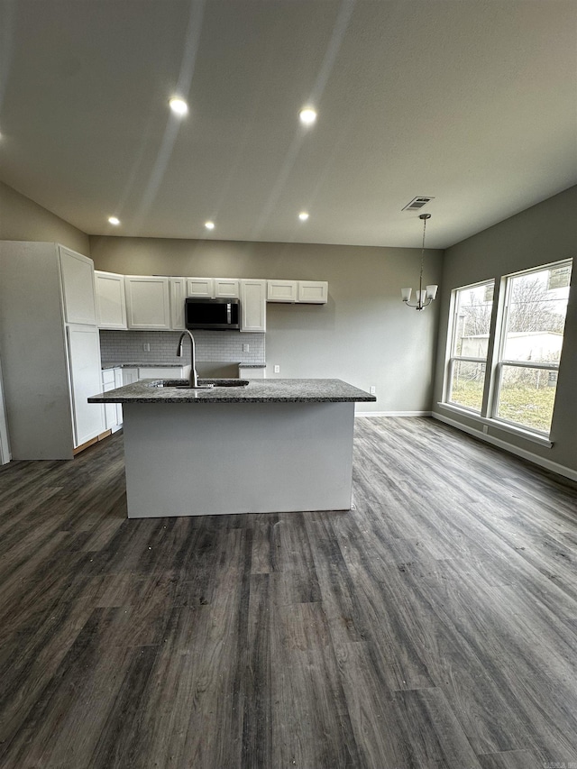 kitchen with pendant lighting, a kitchen island with sink, light stone counters, white cabinets, and dark hardwood / wood-style flooring