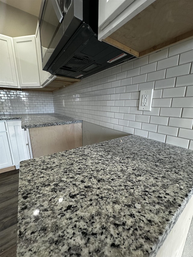 room details with light stone counters, decorative backsplash, and white cabinets