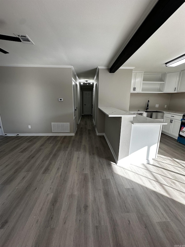 unfurnished living room featuring beamed ceiling, dark hardwood / wood-style floors, ornamental molding, and sink