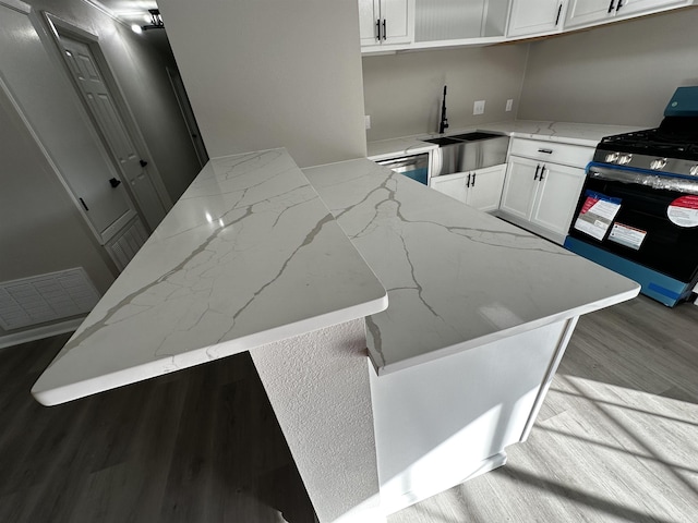 kitchen with kitchen peninsula, light stone countertops, black range oven, sink, and white cabinets