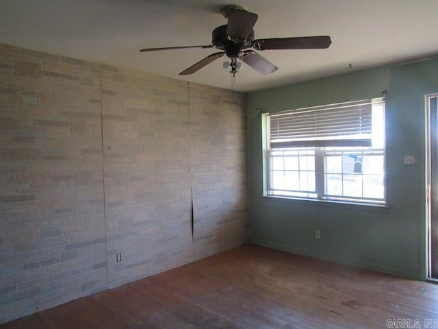 unfurnished room featuring ceiling fan, wood-type flooring, and brick wall