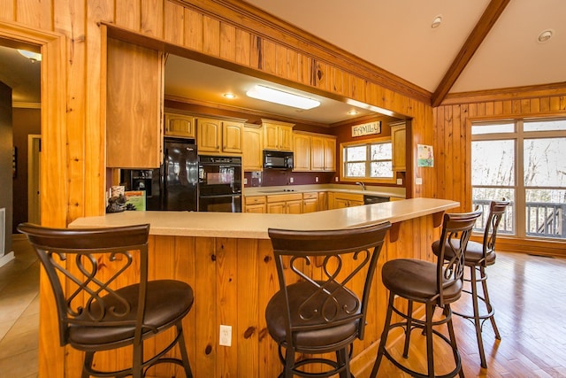 kitchen featuring vaulted ceiling with beams, wood walls, a breakfast bar, and black appliances