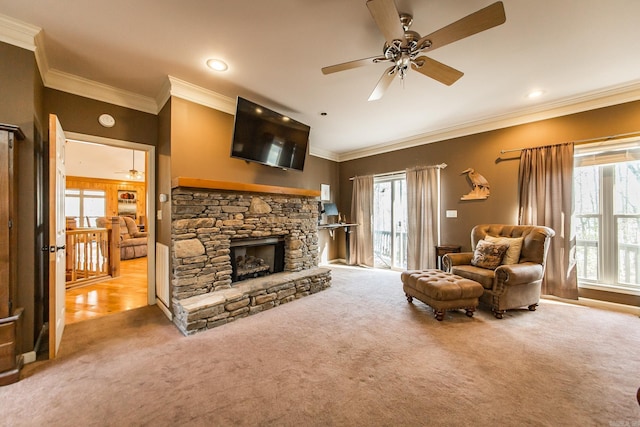 carpeted living room with a stone fireplace, crown molding, and ceiling fan