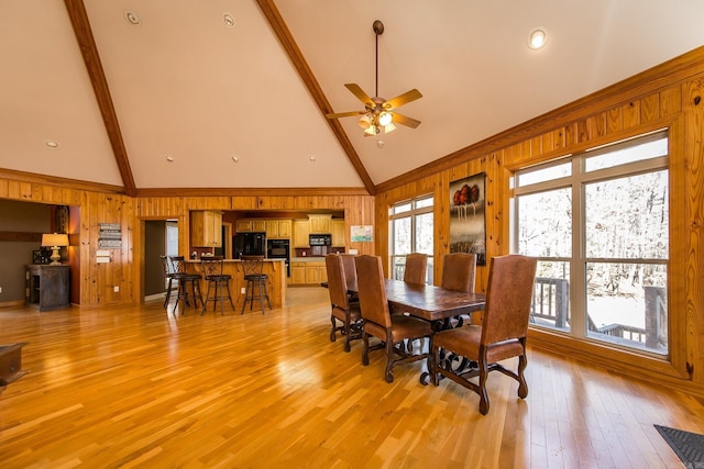 dining room featuring light wood-type flooring, high vaulted ceiling, ceiling fan, and wood walls