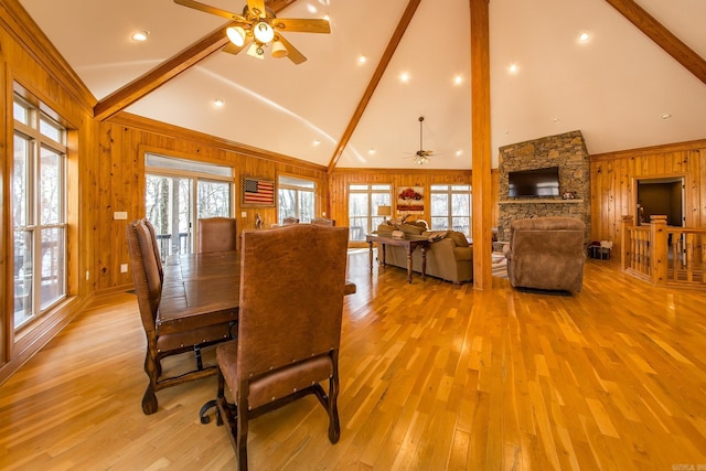 dining room featuring ceiling fan, wooden walls, high vaulted ceiling, light hardwood / wood-style flooring, and beamed ceiling